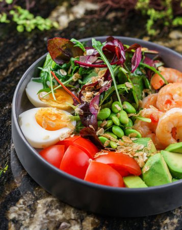 Photo for Buddha bowl salad with shrimps, arugula, spinach, avocado, tomatoes, green edamame beans, eggs on marble background. Healthy salad food, dieting, top view - Royalty Free Image
