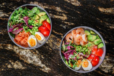 Photo for Two Buddha bowls with salads with shrimps and salmon fish ,arugula, spinach, avocado, tomatoes, green edamame beans, eggs on marble background. Healthy salad food, dieting, top view - Royalty Free Image