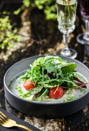 Téléchargez les photos : Salade verte fraîche avec roquette, épinards, tomates cuites au four et sauce sur fond de marbre avec boissons. Alimentation végétalienne saine, manger propre, vue sur le dessus - en image libre de droit