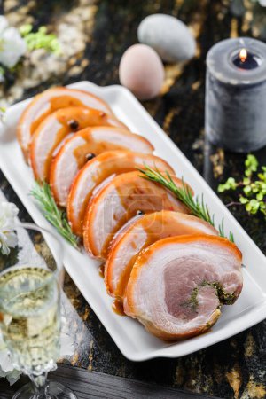 Photo for Holiday baked meat tenderloin with sauce on marble background with wine glasses, candles, easter bunny and eggs. Easter holiday food, top view - Royalty Free Image