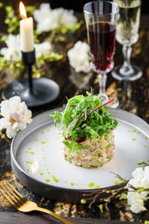 Photo for Salad Olivier with salmon, greens and avocado on marble background with decoration, flowers and wine glasses. Holiday food, top view - Royalty Free Image