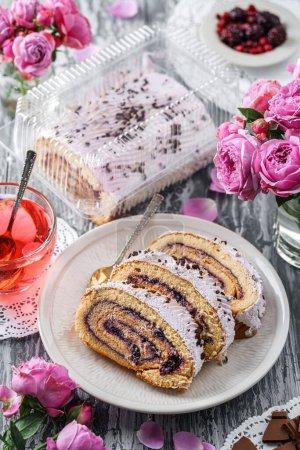 Photo for Delicious sponge roll cake stuffed with cream, berries and chocolate on plate on light grey background with flowers with berries. Sweets, dessert and pastry, top view - Royalty Free Image