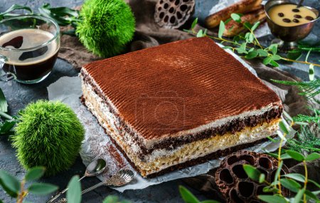 Photo for Tasty cake tiramisu sprinkled with powdered cocoa in grey background with cup of coffee and plants. Sweets, dessert and pastry, top view - Royalty Free Image