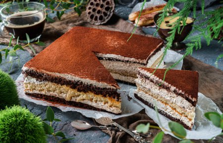 Foto de Sabroso pastel tiramisú espolvoreado con cacao en polvo en fondo gris con taza de café y plantas. Dulces, postres y pasteles, vista superior - Imagen libre de derechos