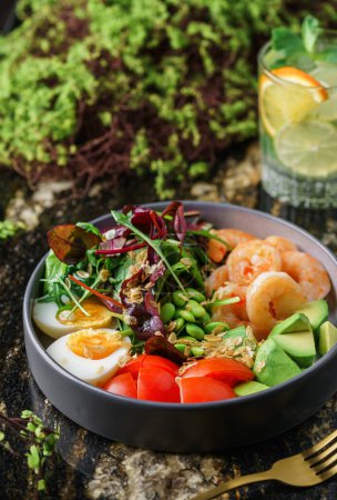 Photo for Buddha bowl salad with shrimps, arugula, spinach, avocado, tomatoes, green edamame beans, eggs on marble background. Healthy salad food, dieting, top view - Royalty Free Image