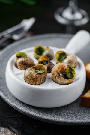 Foto de Deliciosos caracoles marinos con hierbas en plato sobre fondo de mármol. Comida gourmet. Escargot Caracoles, vista superior, primer plano - Imagen libre de derechos