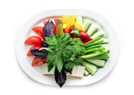 Foto de Surtido de verduras frescas, pepinos, tomates, cebollas, verduras y queso feta en plato aislado sobre fondo blanco. Comida saludable, vista superior - Imagen libre de derechos