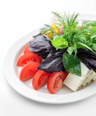 Foto de Surtido de verduras frescas, pepinos, tomates, cebollas, verduras y queso feta en plato aislado sobre fondo blanco. Comida saludable, vista superior - Imagen libre de derechos