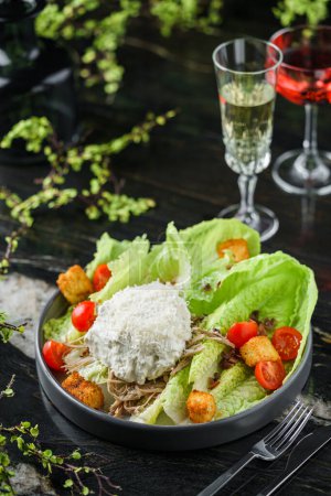 Photo for Fresh vegetable salad with grilled chicken meat, cherry tomatoes, lettuce, crouton and sauce on dark marble table with drinks. Caesar salad, healthy food, close up - Royalty Free Image