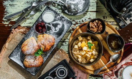 Photo for Delicious breakfast, oatmeal porridge with pieces of fruit, pastry buns with cottage cheese, on rustic background. Top view - Royalty Free Image