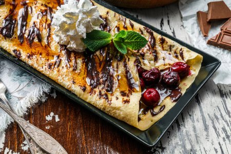 Photo for Crepes with cherries, chocolate and whipped cream on plate on rustic background. Sweets, dessert and pastry, top view - Royalty Free Image