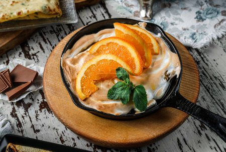 Foto de Merengue con rodajas de naranja y menta en sartén sobre fondo rústico. Dulces, postres y pasteles, vista superior - Imagen libre de derechos