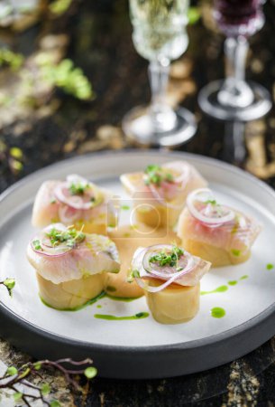Eingelegter Heringsfisch mit Kartoffeln und Soße auf Teller auf Marmortisch mit Weingläsern. Gesundes Essen aus nächster Nähe, von oben