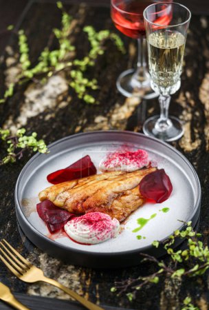 Foto de Filete de pescado dorado al horno con salsa unagi en plato sobre mesa de mármol con copas de vino. Mariscos saludables, primer plano, vista superior - Imagen libre de derechos