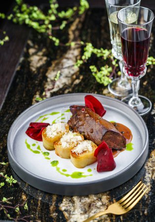 Photo for Tender beef tenderloin meat steak with potatoes and sauce on plate on marble table with wine glasses. Meat food, close up, top view - Royalty Free Image