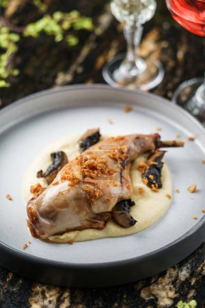 Foto de Carne de conejo al horno con puré de papas y champiñones en plato sobre mesa de mármol con copas de vino. Comida saludable, primer plano, vista superior - Imagen libre de derechos