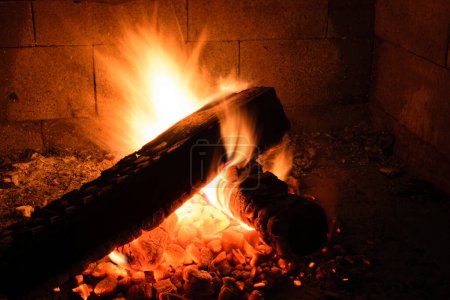 A close-up of a burning log in a fireplace, with flames and embers glowing brightly.