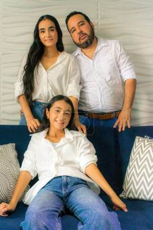 Téléchargez les photos : Parents latino debout tandis que leur mère est assise sur leur canapé à l'intérieur de leur maison - en image libre de droit