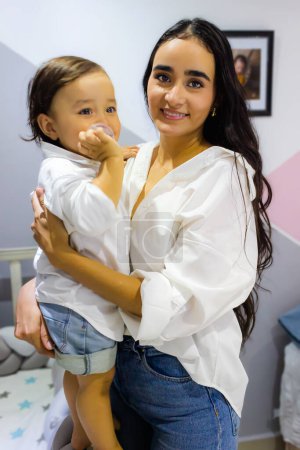 Téléchargez les photos : Maman latine tient son fils bébé et regarde la caméra - en image libre de droit