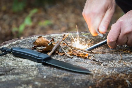 Foto de Manos tratando de encender un fuego con un acero de magnesio en el bosque usando herramientas de bushcraft - Imagen libre de derechos