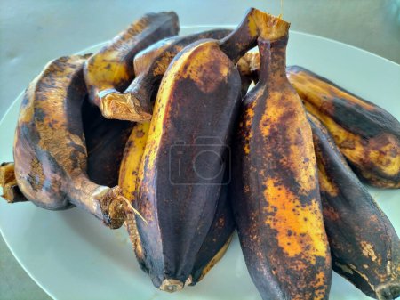 Mehrere gekochte Saba-Bananen werden auf einen weißen Teller gelegt. Asiaten essen gerne gekochte Bananen mit heißen Getränken zum Frühstück.