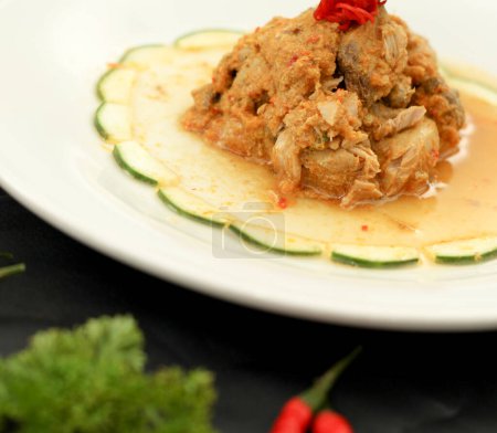 Cakalang Rica - Spezialnahrung aus Manado Indonesia, hergestellt aus Skipjack-Fisch, der in würzigem aromatischem Sambal gekocht wird. Serviert auf weißem Teller. Seitenansicht.