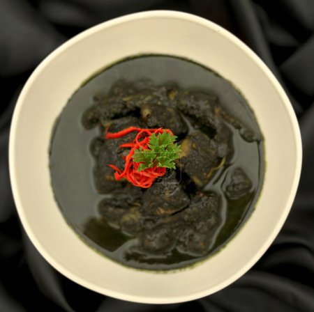 Nourriture indonésienne, Calmar à l'encre noire - Les meilleurs plats de fruits de mer d'Indonésie, avec de l'encre de calmar, du poivre, de l'ail, du piment dans un bol blanc sur fond noir. Vue du dessus.