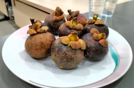 Mangostán (Garcinia mangostana), también conocido como el mangostán púrpura, familia Clusiaceae. Grupo de frutos del mangostán en plato blanco. Enfoque selectivo.