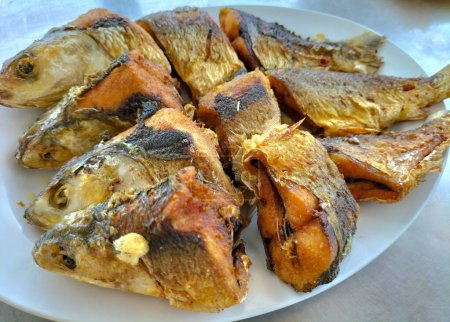 Gebratener Milchfisch, trocken mit Kurkuma gewürzt, als indonesisches Hausgericht. Serviert auf einem Teller. Selektiver Fokus.