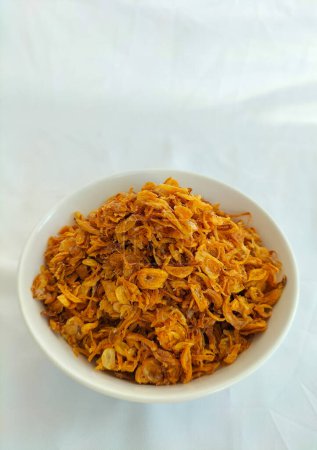 Frittierte Schalotten zum Garnieren in einer weißen Schüssel. Diese gebratenen Schalotten sind ein Gewürz, das häufig als Aroma auf verschiedenen indonesischen Gerichten verwendet wird. Rote Zwiebel. Selektiver Fokus.