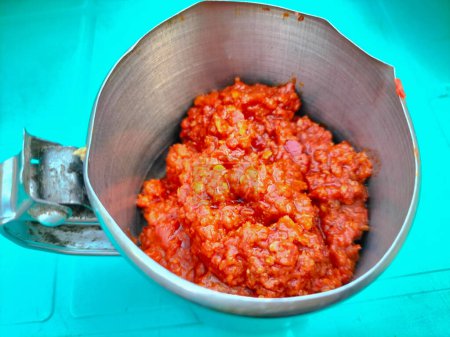 Selektiver Fokus von rotem Chili. Traditionelle indonesische scharfe Chilisoße. Chilisoße in einer kleinen Tasse auf grünem Hintergrund.