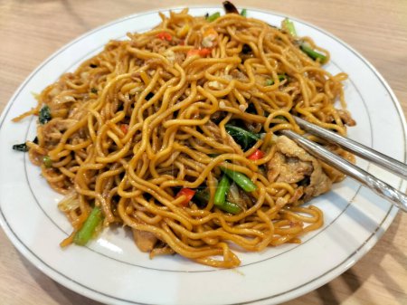 Close up view of stir fry noodles with vegetables and shrimps in white plate. Spicy stir fried noodle with chopsticks.