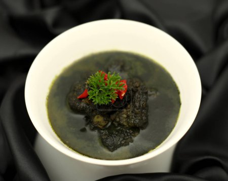 Indonesia food, Squid in black ink sauce - The best  seafood dishes in Indonesia, with squid ink, pepper, garlic, chilli in a white bowl on a black background. 
