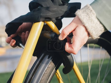 Un detallado primer plano que muestra una mano bloqueando el marco de una bicicleta amarilla, enfatizando la acción de asegurar la bicicleta, con un enfoque en el mecanismo de bloqueo y la rueda de la bicicleta