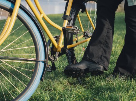 A detailed shot captures a person's foot lifting the kickstand of a yellow bicycle, preparing to ride off on a grassy field