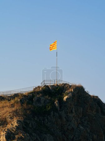 The iconic Catalan flag flies proudly atop the historic Sant Joan hill in Blanes against a clear sky