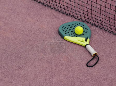 Close-up of a neon green padel racket with a yellow ball on a purple textured court surface