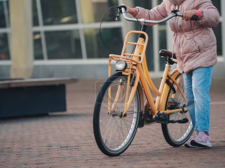Nahaufnahme eines jungen Mädchens mit einem gelben Fahrrad auf einem Kopfsteinpflaster-Weg, das den nachhaltigen städtischen Verkehr hervorhebt