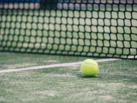 Ein lebhafter Tennisball, der nahe der weißen Begrenzungslinie auf einem grünen Platz steht, im Hintergrund verschwommenes Netz