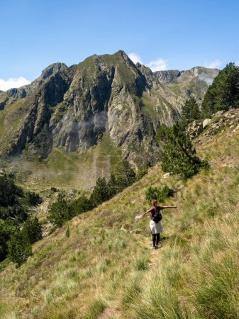 Una mujer de pelo rizado extiende sus brazos, balanceándose en un estrecho sendero con un increíble telón de fondo de montaña