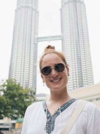 Mujer con gafas de sol y un top blanco sonriendo frente a las icónicas Torres Petronas en Kuala Lumpur, Malasia
