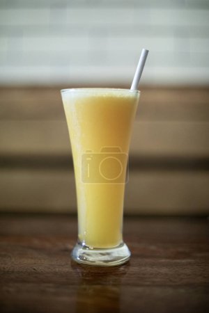 Foto de Una foto de cerca de un vaso de jugo de naranja con una sola pajita delgada que sale del centro. El jugo es de un color naranja vibrante, con pequeñas burbujas de aire brillando a lo largo - Imagen libre de derechos