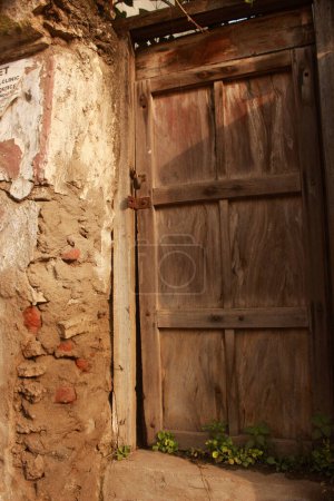 Téléchargez les photos : Une porte en bois altérée avec peinture pelante est installée dans un mur de briques rustique - en image libre de droit