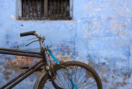 Téléchargez les photos : A classic bicycle with a brown leather seat and handlebars rests against a weathered blue wall. The bicycle has cream colored tires and a silver fram - en image libre de droit
