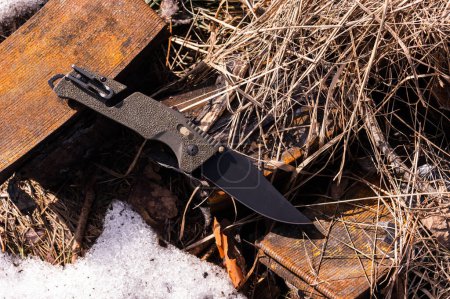 Photo for Folding knife with many tools. Multifunctional knife for the military. Knife lying on hay and rusty iron. Knife with clip. View from above. - Royalty Free Image