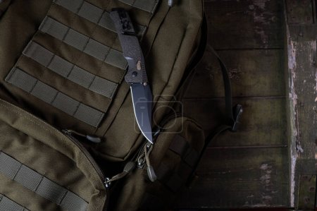 Photo for Folding sharp army knife on a military backpack. Knife with clip and safety. Backpack with molle ribbons. Military composition. View from above. - Royalty Free Image