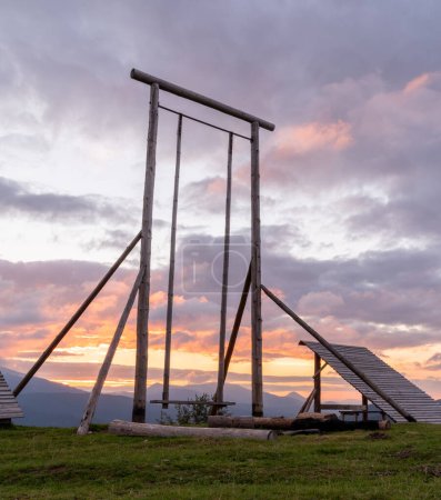 Foto de Large wooden swing on top of the mountain. Wooden swing against the background of the sunrise. Vertical frame. - Imagen libre de derechos
