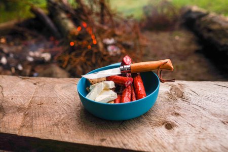 Photo for Folding knife with wooden handle. Knife and cut sausages and cheese. Snack outdoors by the fire. Knife and sausages on the bench. - Royalty Free Image