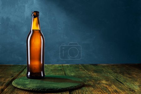 Photo for Brown glass bottle. The bottle is on a tray on the table. Blue background. Copy space. Front view. - Royalty Free Image