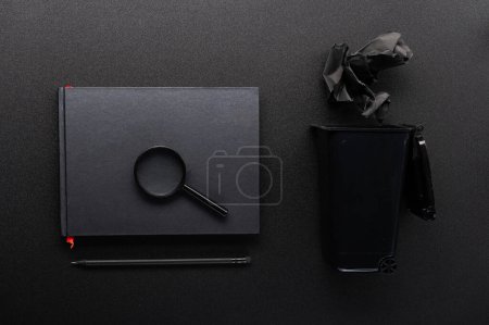 Foto de Lupa en un bloc de notas. Composición de objetos negros. Cuaderno y cubo de basura. Búsqueda de información. - Imagen libre de derechos